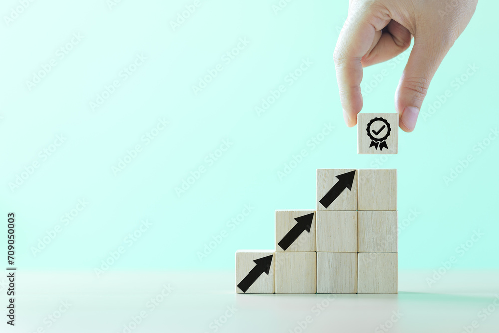 Poster hand-putting a symbol of quality assurance and arrow increasing on wooden cube for quality enhanceme