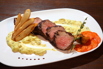 Steak medium roast, cut into pieces in creamy mushroom sauce. Steak served on a white plate and wooden table.