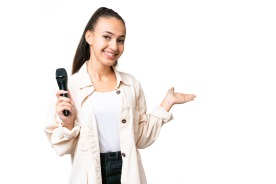 Young singer woman picking up a microphone over isolated chroma key background extending hands to the side for inviting to come