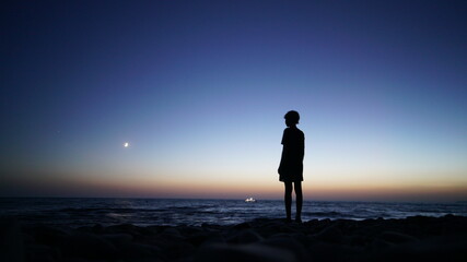 silhouette of a boy against the backdrop of the sea and lunar landscape