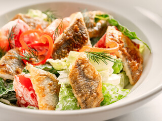 Delicious salad with fried baked smelt fish. Fried fish salad with fresh green lettuce, tomatoes,...