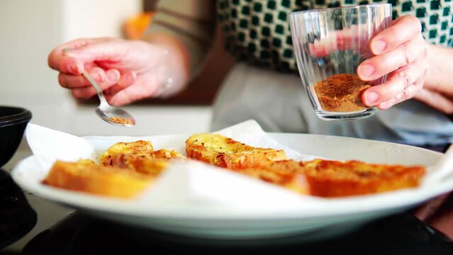 Mujer mayor irreconocible espolvoreando az&uacute;car y canela sobre el pan para la receta de torrijas de Semana Santa
