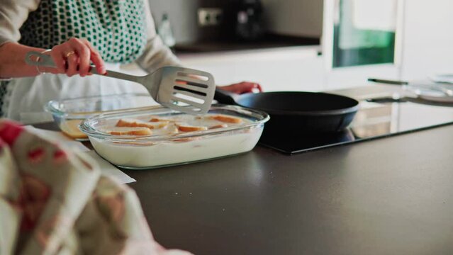 Mujer mayor en la cocina remojando pan en leche y huevo para hacer torrijas tradicionales para su familia en las fiestas de semana santa