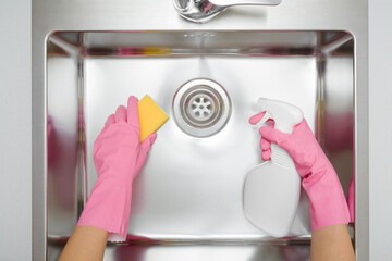 Woman hands in pink rubber protective gloves holding white spray bottle and yellow sponge and...