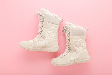 New beige warm winter boots with shoelace on light pink table background. Pastel color. Female...