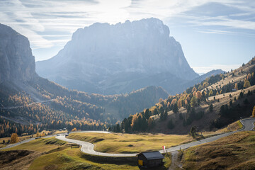 Road curving in high alpine pass with prominent mountain and woods in fall colors, Dolomites, Italy