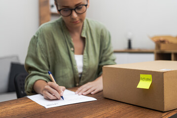 woman writes a return order at home, her determination evident as she fills out the form to return a purchased item. 