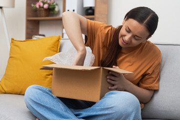 Brunette woman consumer takes out clothes from open cardboard box in premise of apartment concept...