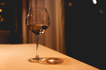 One elegant glass of white wine on high stem on light color table.