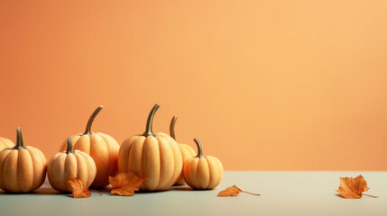 A minimalist autumnal display featuring small pumpkins arranged on an orange backdrop, with scattered dry leaves.