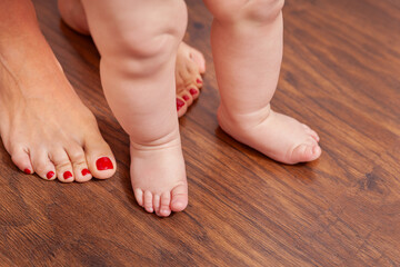 The close plan of the legs of the baby and mother. First steps. Mom helps the child