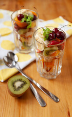View from the top to large transparent glasses with chopped fruits and berries and long spoons on the table. Mandarin, kiwi, banana, strawberries, blueberries, cherries and mint leaves. Healthy snack.