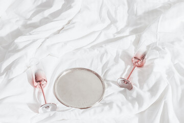 Pink color shining champagne glasses on bed, on white blanket. Lifestyle aesthetic photo, star...