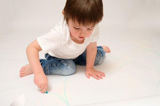 Toddler baby learn to draw on paper, studio white background. The child draws with a pencil.