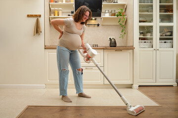 A woman suffering from backache due to pregnancy is cleaning the kitchen with a wireless vacuum....