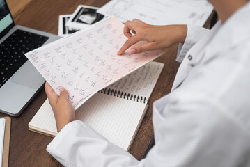 Young doctor reads papers with results of patient cardiogram tests female cardiologist examines...