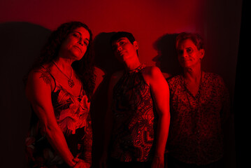 Three pretty female musicians wearing colorful clothing leaning against a wall.