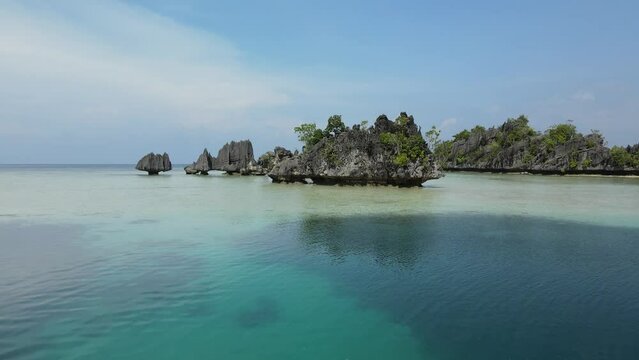 aerial shoot, flight over colourful lagoon with Turquoise water, sand beach and palm trees in Raja Ampat Indonesia