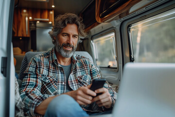 A handsome man in stylish clothes works with a laptop in a trailer, motor home. Freelancer. Work remotely. trailer home. Camping vacation