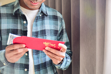 Cropped image of a South Asian man holding a red envelope or hongbao with Taiwan currency thousand...