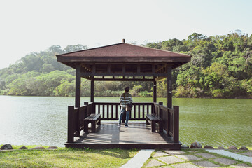 Gazebo in the park. A South Asian traveller enjoying nature from a lakeside viewpoint on a sunny...