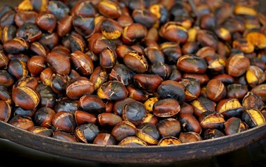 Fried chestnuts in a pan on a wooden stand, flat lay. Fresh roasted chestnuts for christmas or holidays, seasonal dish