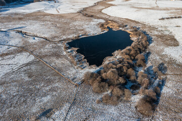 Aerial view of a lake in winter with ice, snow and nearby road close to a mountain