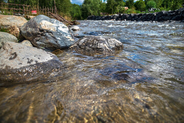 Landscape of a mountain river against the background of a forest, a pine forest along the banks, stones in the channel, a mountain stream, summer heat