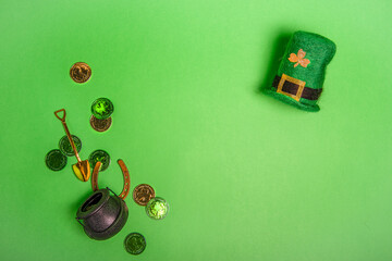 Top view on a green isolated background lie St. Patrick's hat, leprechaun pot with gold coins,...