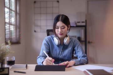 Young asian student women studying and watching lecture webinar in lesson online class to writing notes on digital tablet while doing homework and learning knowledge remote education from home