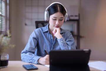 Young asian student women wearing headphone to studying lecture webinar in online class on tablet...