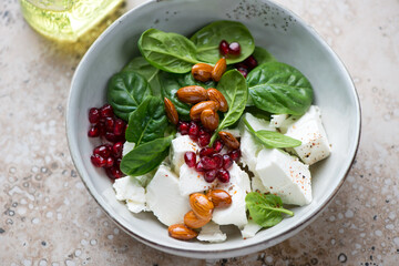 Salad with fresh spinach, feta cheese, pomegranate seeds and almonds served in a grey bowl, horizontal shot, middle close-up