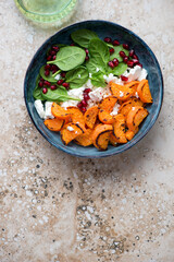 Blue bowl with roasted sweet potato, fresh spinach, feta and pomegranate, above view on a beige granite background, vertical shot with space