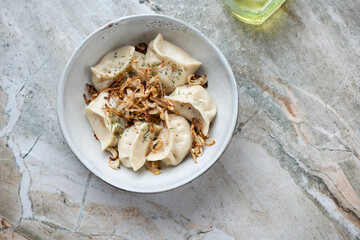 Bowl of vareniki or stuffed dumplings served with fried onion, above view on a grey granite background, horizontal shot with space © Nickola_Che