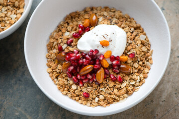 White bowl with granola, greek yogurt, pomegranate seeds and nuts, middle closeup, selective focus, horizontal shot