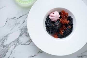 Black spaghetti with baby octopus and red caviar served in a white plate, top view on a white...