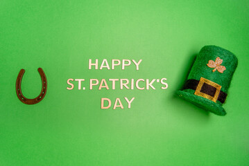 Horizontal banner with Happy St. Patrick lettering on green isolated background with green leprechaun hat with golden shamrock, lucky horseshoe. Traditional Irish symbols. Copy space