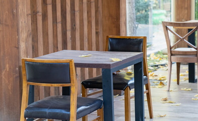 Table and chairs on the terrace of an empty street cafe in late autumn, end of the season. Yellow maple leaves scattered on the tables and the wooden floor of the cafe terrace.