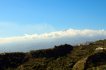 Panoramic nature landscape. Mountains against blue sky. Famous Sicilian Etna volcano in white clouds in the background. View from Taormina. Travel and tourism concept