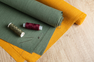 Sewing background, green and orange fabric, threads with needles on wooden table - 709123408