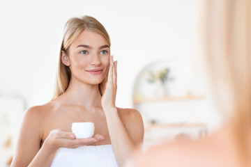 Fototapeta na wymiar Pretty blonde lady indulges in facial skincare moisturizing face indoor