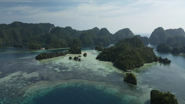 aerial shoot, flight over colourful lagoon with Turquoise water, sand beach and palm trees in Raja Ampat Indonesia