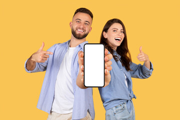 Happy couple showing smartphone screen with thumbs up on yellow backdrop
