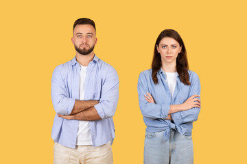 Two young adults in casual attire, standing with arms crossed on yellow background