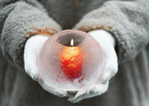 Handmade ice globe lantern with red candle burning in the girls hands. Winter craft and Ice art or outdoor decoration concept. - Powered by Adobe