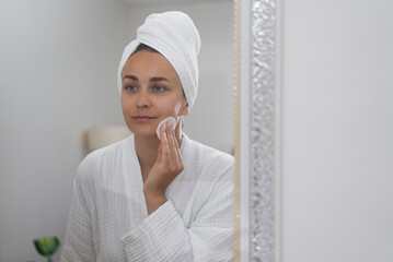 woman, by the bathroom mirror, practices self-care, gently cleansing her skin with a cotton pad. 