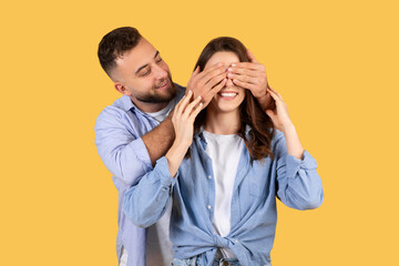 Man covering woman's eyes with hands, both smiling