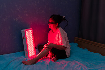 Senior woman treating sore leg with the red light therapy panel