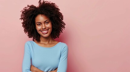 Young African American girl light blue long sleeve top smiling, holding her arms folded and looking at camera isolated on pastel pink background