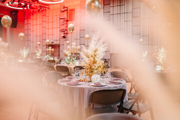 festive event space with tables set with golden centerpieces, balloons, and a stage with red lighting, all seen through a soft focus filter.
